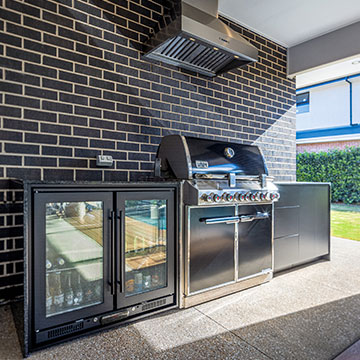 Fridge, BBQ and cabinets with rangehood against dark brick wall